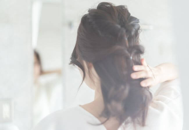 梅雨の時期の湿気で髪がまとまらないのでまとめ髪のスタイルにヘアセットしている女性のイメージ画像です。